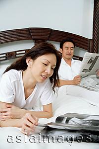 Asia Images Group - Couple in bedroom, woman reading magazine, man reading newspaper