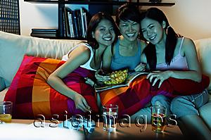 Asia Images Group - Three young women in living room, sitting on sofa, smiling at camera