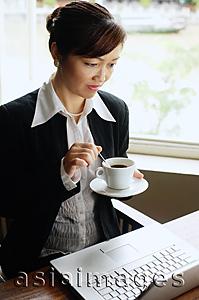 Asia Images Group - Businesswoman looking at laptop, holding cup and saucer