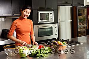 Asia Images Group - Woman cutting vegetables in kitchen, smiling at camera, portrait
