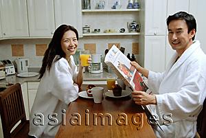 Asia Images Group - Couple having breakfast, smiling at camera, man holding newspaper