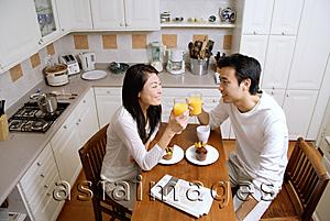 Asia Images Group - Couple in kitchen, having breakfast, holding glasses of orange juice