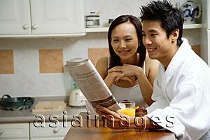Asia Images Group - Couple in kitchen, having breakfast, looking at newspaper