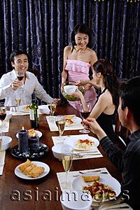 Asia Images Group - Couples having dinner party at home, woman serving food