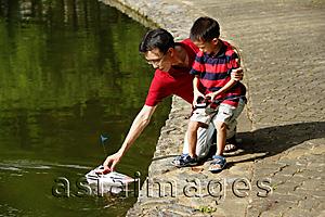Asia Images Group - Father and son playing with remote control boat, father reaching for boat