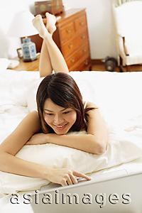 Asia Images Group - Woman in bedroom, lying on bed, using laptop