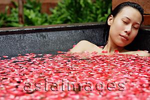 Asia Images Group - Woman in tub with floating rose petals, eyes closed