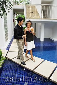 Asia Images Group - Couple walking by swimming pool, champagne glasses in hand