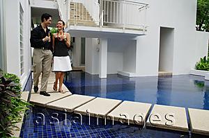 Asia Images Group - Couple walking next to swimming pool, champagne glasses in hand