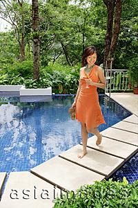 Asia Images Group - Woman walking by swimming pool, holding glass of champagne and carrying sandals