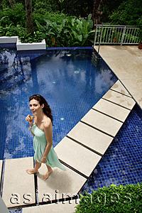 Asia Images Group - Woman in green dress walking around swimming pool, looking up at camera