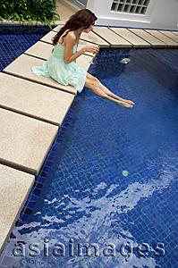 Asia Images Group - Woman in green dress sitting by pool, legs in the water