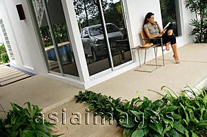Asia Images Group - Woman sitting on patio, reading magazine