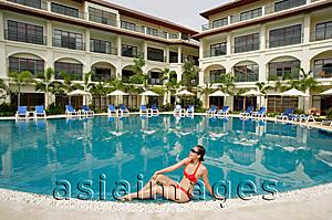 Asia Images Group - Woman sitting next to swimming pool, wearing bikini, hand on knee