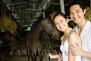 Asia Images Group - Couple in stable, standing with horse, looking at camera