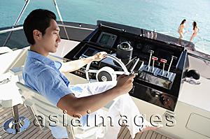 Asia Images Group - Man at helm of yacht, people in the background