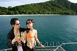 Asia Images Group - Couple on boat deck, standing next to railing, toasting champagne glasses