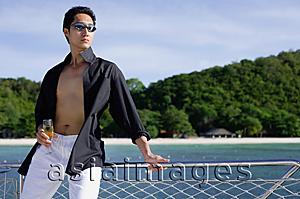 Asia Images Group - Man on boat, leaning on railing, drink in hand