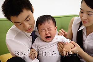 Asia Images Group - Father holding crying baby boy, mother sitting next to them