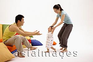 Asia Images Group - Father sitting on sofa, arms outstretched, mother helping toddler walk towards him