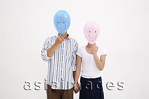 Asia Images Group - Couple standing side by side, holding hands, with balloons over their faces