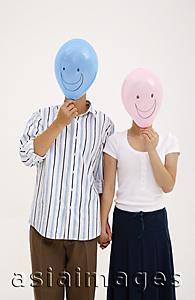 Asia Images Group - Couple holding hands, with balloons over their faces