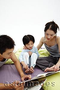 Asia Images Group - Family with one child sitting on bed, looking at book