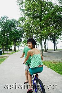 Asia Images Group - Couple cycling on tandem bicycle, woman looking over shoulder