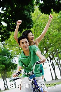 Asia Images Group - Couple on tandem bicycle, woman raising arms in the air