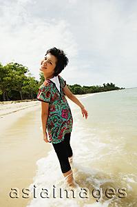 Asia Images Group - Woman walking on beach, looking over shoulder