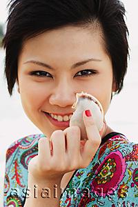 Asia Images Group - Woman holding shell, smiling at camera, portrait