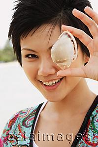 Asia Images Group - Woman holding shell over one eye, smiling at camera