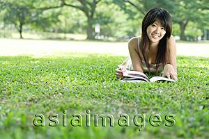 Asia Images Group - Young woman lying on grass in park, looking at camera