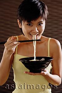 Asia Images Group - Young woman with chopsticks, eating noodles, looking at camera