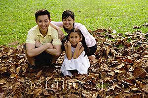 Asia Images Group - Family with one child crouching on pile of leaves, looking at camera
