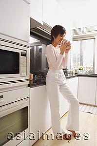 Asia Images Group - Young woman standing in kitchen, drinking coffee