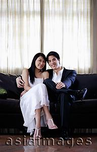 Asia Images Group - Couple sitting side by side on sofa, smiling at camera