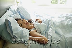 Asia Images Group - Woman lying in bed, smiling at camera