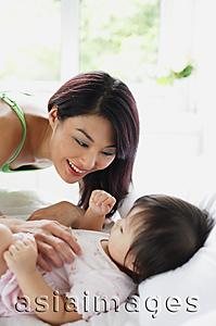 Asia Images Group - Baby girl lying on bed, mother leaning over her