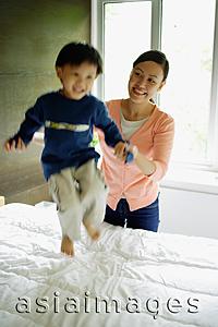 Asia Images Group - Young boy jumping on bed, mother holding his hand