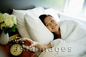 Asia Images Group - Woman reaching for alarm clock on bedside table