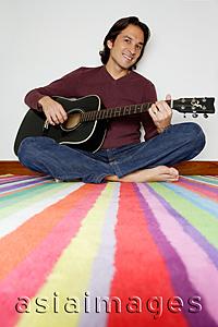 Asia Images Group - Man sitting on striped carpet, holding guitar, smiling at camera