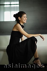 Asia Images Group - Young woman in black dress, crouching, looking away