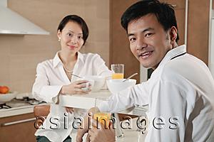 Asia Images Group - Couple sitting in kitchen with breakfast, looking at camera