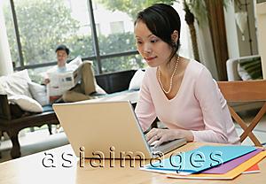 Asia Images Group - Woman using laptop, man in background reading newspaper