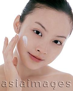 Asia Images Group - Young woman looking at camera, applying moisturizer on face