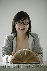Asia Images Group - Young woman smiling at camera, open book in front of her