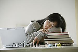 Asia Images Group - Young woman sleeping on stack of books, laptop open next to her
