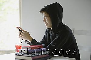 Asia Images Group - Young man with hooded jacket, looking at mobile phone