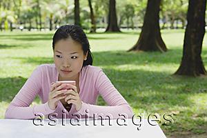 Asia Images Group - Young woman sitting at outdoor table, holding coffee cup, looking away